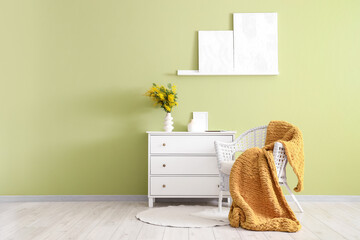 Interior of room with armchair, commode and mimosa flowers in vase