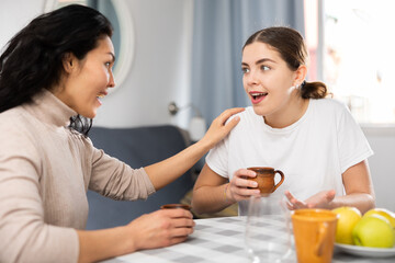 Two women talking and drinking tea while sitting at table in apartment.