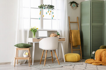 Interior of office decorated for Easter with workplace, ladder and folding screen