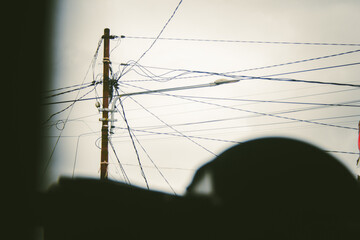 Electric pole with messy cables against the cloudy sky