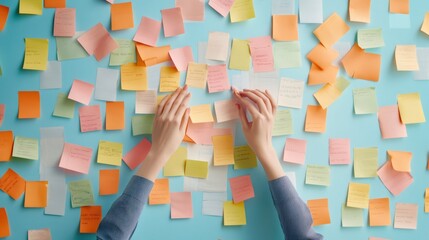 Hands sorting through a chaotic array of colorful sticky notes on a blue background, symbolizing multitasking, time management, and stress in a fast paced work environment