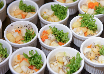 Fresh Fruit Salad in Arranged White Ramekins. The fruit salad includes diced tropical fruits such as dragon fruit, pineapple, papaya, melon, garnished with green lettuce and black sesame seeds.