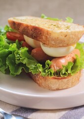 Sourdough bread open faced sandwiches with lettuce, tomatoes, egg and sausage. A healthy and delicious breakfast.
