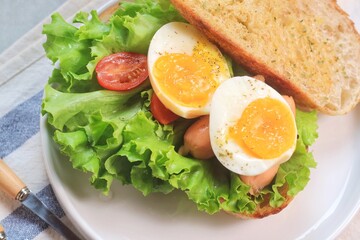 Sourdough bread open faced sandwiches with lettuce, tomatoes, egg and sausage. A healthy and delicious breakfast.
