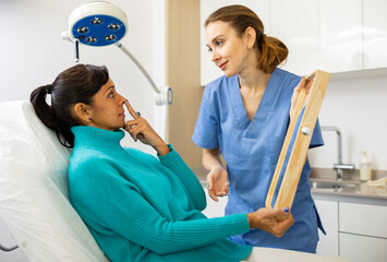 Skilled female beautician giving consultation to woman patient with mirror in aesthetic clinic