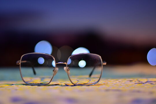 Eye glasses with dramatic background, Glasses at night, Eyeglasses resting on a floor during sunset, A pair of glasses, Black glasses have a male hand with a vintage bokeh background
