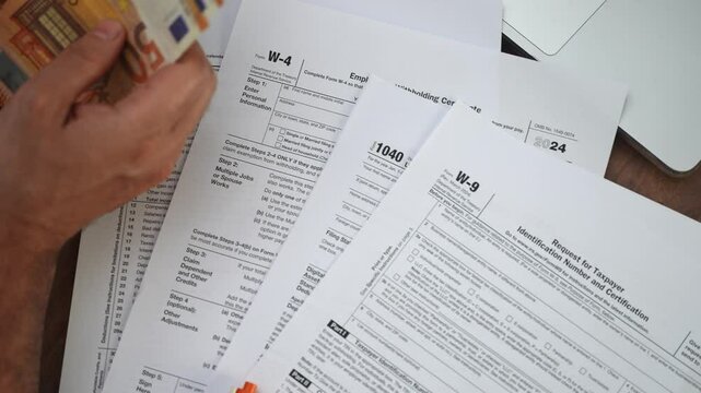 Self-employed man scrupulously counts money sitting at table with uncompleted W-4 1040 and W-9 tax declarations office documentation concept slow motion