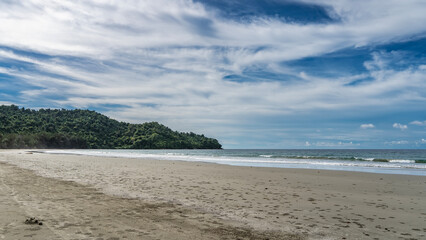 Beautiful tropical beach. Footprints on the sand. The waves of the turquoise ocean are foaming. A green hill in the distance. Blue sky, clouds. There are no people. Malaysia. Borneo. Kota Kinabalu