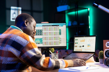 Entrepreneur doing remote work using monthly revenue balance, examining statistics at his...