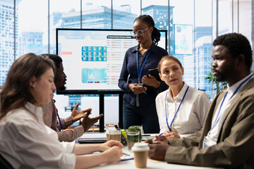 Marketing specialist using monthly infographics on interactive board in a status update meeting,...
