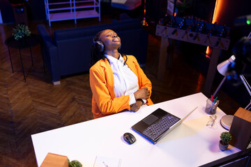 Cheerful teenager in neon lit apartment listening music during leisure time, feeling pleased. Jolly...