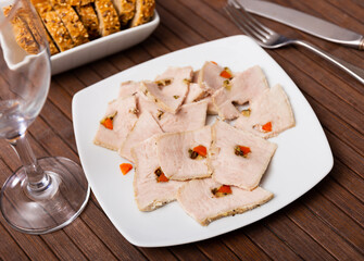 Slices of homemade ham from boiled pork stuffed with carrot small cube bits are beautifully laid out on plate. Homemade ham is complemented by plate with slices of bread