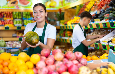 Young female seller working in a vegetable store puts melons on the counter