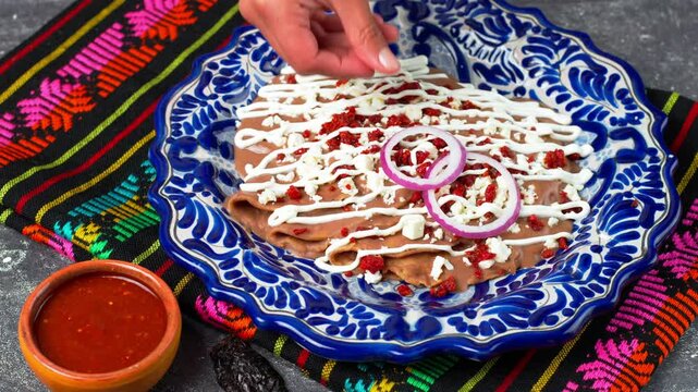 Mexican Enfrijoladas, hands of a Mexican woman place red onion rings on top of enfrijoladas dipped in bean sauce