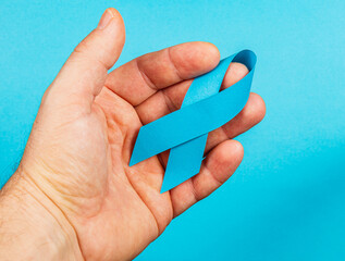 Hand holding a blue ribbon symbolizing cancer awareness and support for men