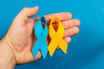 Hand holding blue and yellow awareness ribbons for health campaigns