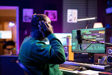 African american music producer listening to recorded song in home studio, making room for...