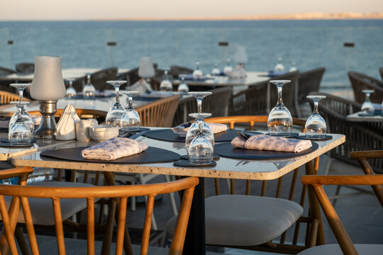 Elegant seaside dining setup with glassware, overlooking the ocean at sunset.