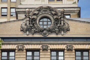 A richly ornamented window graces a weathered brick facade in New York, Manhattan. The...
