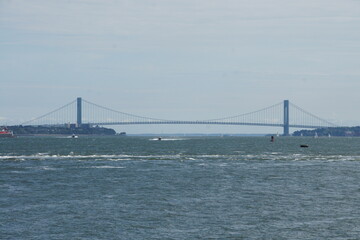 New York, Manhattan's iconic skyline stretches across the East River, dwarfed by the majestic Verrazano-Narrows Bridge in the distance. This suspension bridge connects Staten Island to Brooklyn, a