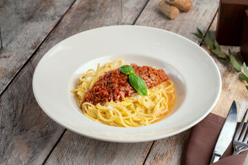 Pasta Bolognese – A delicious Italian dish featuring spaghetti topped with rich, savory Bolognese sauce and fresh basil, served on a white plate on a rustic wooden table with wine 