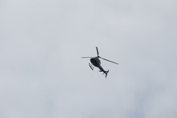 A red and white helicopter soars through a sea of fluffy clouds above New York, Manhattan. Challenging weather conditions create a dramatic scene from the air.