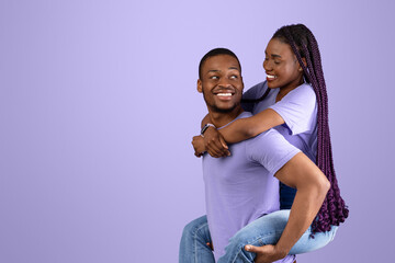 Piggyback Ride. Smiling black man carrying and riding his woman with long afro braids on back,...