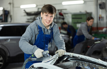 Guy auto mechanic performs car body work in auto repair shop. Auto mechanic young woman polishes...
