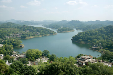 Fototapeta premium Serene aerial view of a picturesque lake nestled within lush green mountains, showcasing a tranquil village and traditional architecture.