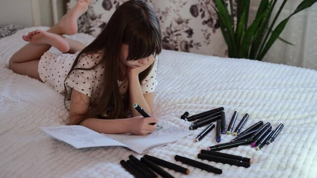 Portrait of teenage girl drawing with colored pencils on bed at home. Child spends time being creative and drawing.