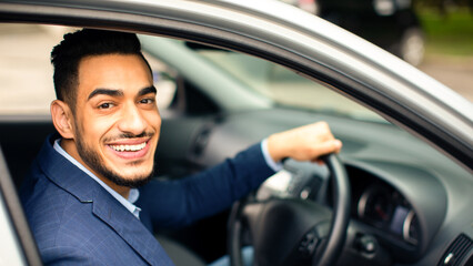 Happy handsome middle-eastern businessman driving car, going to business trip, side view, copy space. Arab man in stylish outfit going to business meeting or to office, driving his luxury car
