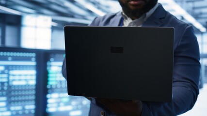 Technician in server hub using laptop to patch network issues leading to slow data transfer rates. Close up of IT professional in data center fixing errors affecting supercomputers, camera B