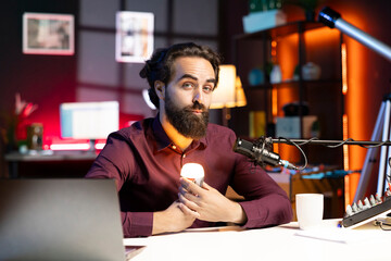 Content creator holding smart light bulb under face to create creepy mood in studio while telling...