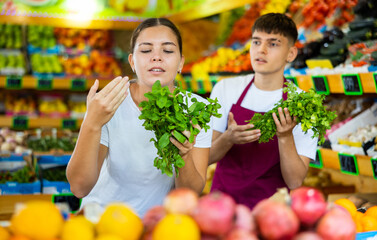 Friendly guy seller helps a girl buyer who came to the store for shopping, choose a fresh greenery