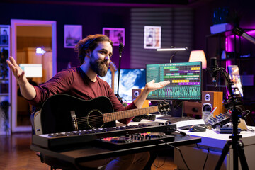 Songwriter recording himself in home studio singing and playing guitar, filming video about...