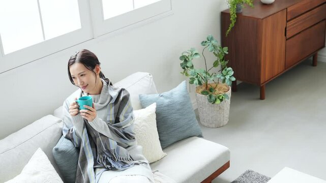 女性、飲む、寒い、冬、暖かい、コーヒー、笑顔、日本人、暖冬、対策、防寒、ストール、ショール、ブランケット、コピースペース、インテリア、リビングルーム、ライフスタイル、おしゃれ、リラックス、ほっこり、安心、ソファー、若い、寒暖差、紅茶、カップ、暖房、エアコン、マフラー、ポジティブ、快適、節電、室内、明るい、省エネ、爽やか、毛布、シンプル、キレイめ、きれいめ、寒さ、寒気、冷気、住宅、俯瞰、ハイアングル