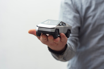 Silver Electric Car miniature held in hand, futuristic design on white background.
