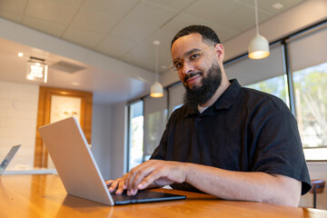 Fototapeta premium A content African American man engages with his laptop in a bright, modern caf setting. The relaxed atmosphere enhances his focused demeanor
