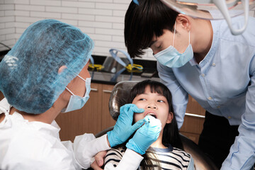 Obraz premium Asian female pediatric dentist examines a girl's teeth in dental clinic and takes care and encourages of father, mouth oral hygiene, and professional orthodontic healthcare work in a kid hospital.