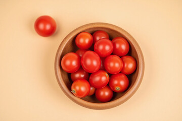 small wooden bowl filled with red cherry tomatoes beige background