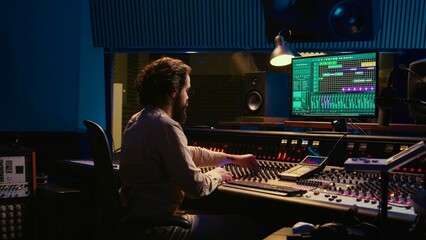 Control room sound engineer editing music with sliders and knobs, working on post production in professional soundproof studio. Technician producing songs on stereo mixing console. Camera B.