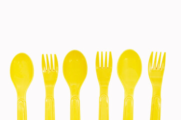 Yellow plastic camping spoons and forks laid out in a row on a white background, copy space