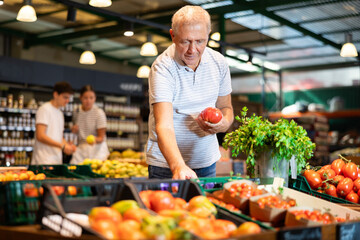 Elderly man shopper choosing tomatoes in grocery store