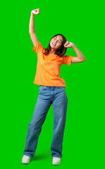 Young woman in orange shirt happily dancing against bright green background during a joyful moment