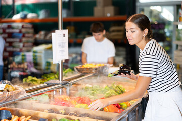Young woman shopper choosing eggplants in grocery store