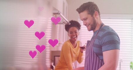 Image of hearts over diverse couple cooking together and drinking wine in kitchen at home