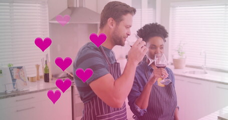 Image of hearts over diverse couple cooking together and drinking wine in kitchen at home