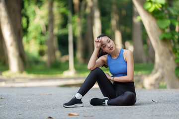 Young asian sportswoman wiping sweat from her forehead while resting in a green park after an...