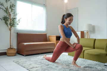 Obraz premium Happy athletic woman practicing yoga, enjoying fitness lifestyle, exercising at home, wearing sportswear, stretching legs on carpet in living room, training muscles, improving flexibility