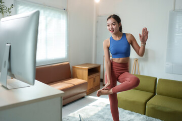 Young woman engages in a yoga session at home, following instructions from a computer screen. The cozy living room setting enhances the peaceful atmosphere of her practice